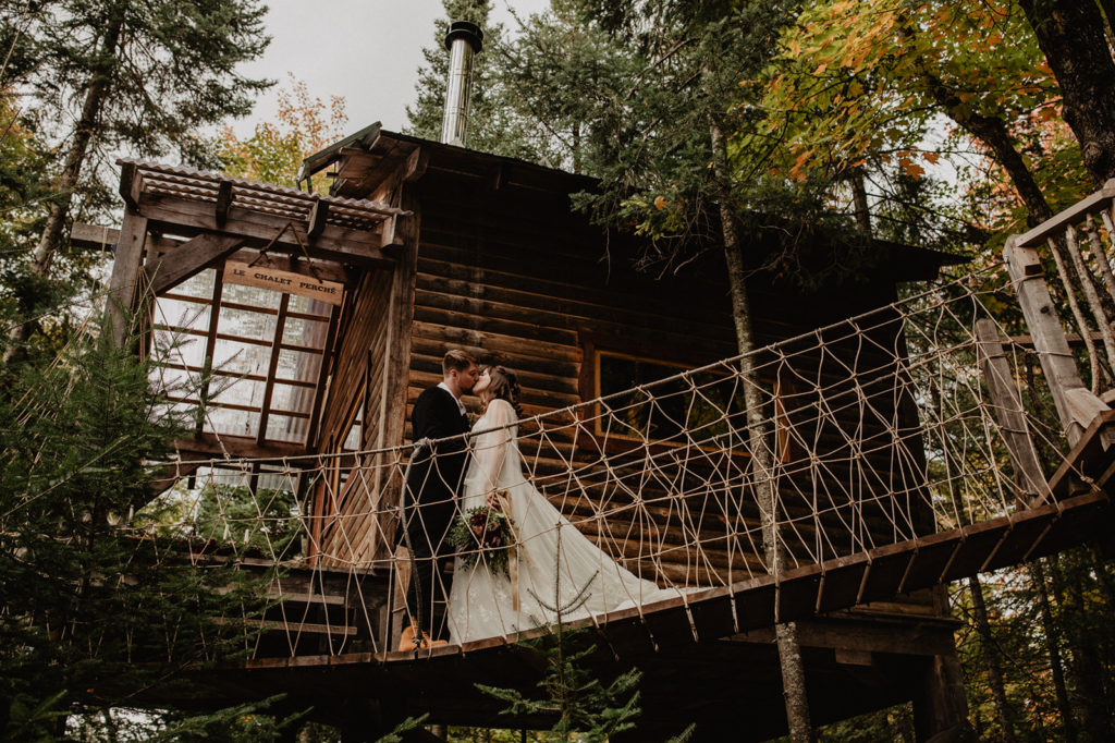 Treehouse Chalet in Quebec with couple in wedding attire kissing on a suspension bridge 