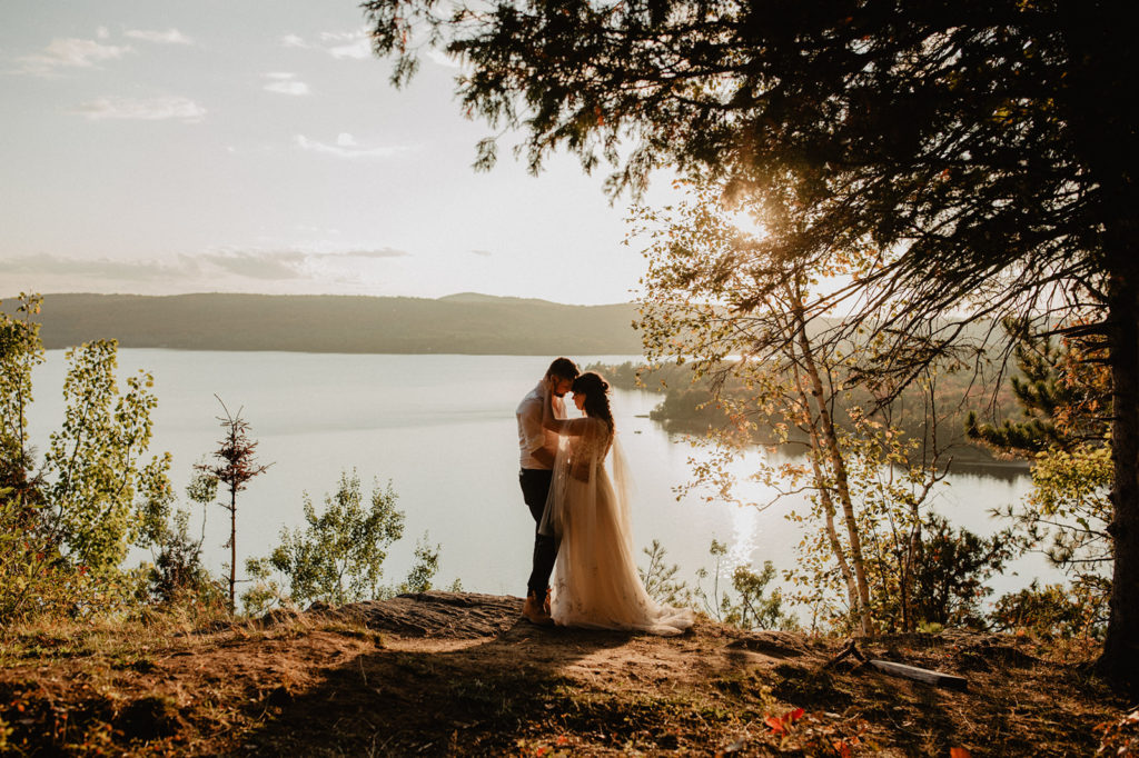 Couple in wedding attire overlooking a lake at sunset